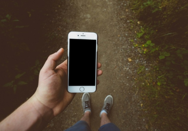 Man houdt telefoon in smartphone hoesje vast op grindpad